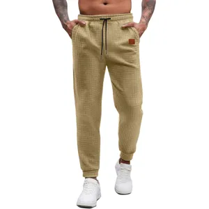 Men's khaki waffle knit sweatpants detailed view, featuring elastic drawstring waist and cuffed ankles.