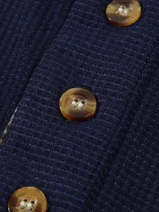 Close-up detail of dark blue waffle knit fabric with brown buttons and neat stitching.
