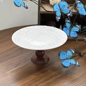 White ceramic footed cake stand with embossed scroll pattern and wooden base for dessert display.