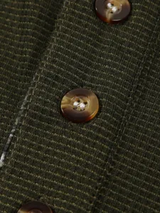 Close-up detail showcasing the olive green waffle knit texture and tortoiseshell button.