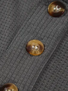 Close-up detail of dark grey waffle knit fabric with brown buttons, textured clothing texture.