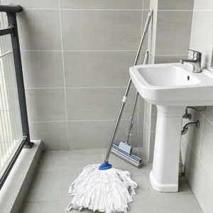 Dettaglio di un mocio per la casa e un mocio in spugna appoggiati a una parete piastrellata.