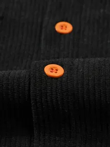 Détail de tissu de chemise en velours côtelé noir avec des boutons oranges contrastés.
