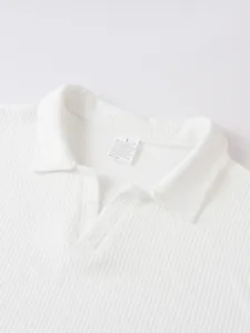 Detailansicht des gerippten Strickkragens an einem weißen Herren Polohemd mit Etikett.