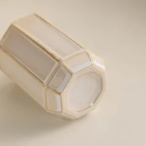 Close-up detail of modern minimalist ceramic faceted tumbler cup in elegant cream beige finish.