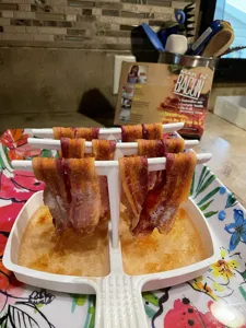 Close-up detail view of the microwave bacon rack in use, holding crispy cooked bacon on rods.