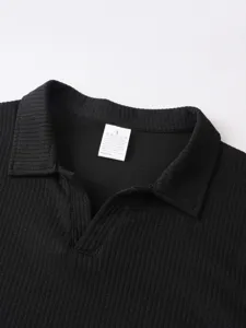 Nahaufnahme des Kragens eines schwarzen Rippstrick-Poloshirts mit Etikett und Größe.