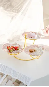Detalle exquisito de plato de postre con concha de perla y soporte dorado de cerámica rosa elegante.