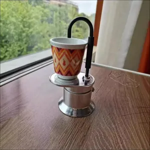 Vue detaillee de la mini cafetiere moka portable en aluminium avec tasse coloree et bras verseur.