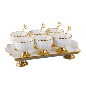 Detailed view of white ceramic pedestal bowl set with gold trim and matching spoons on tray.