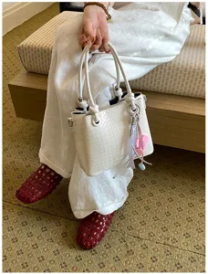 Detailed view of a stylish white woven bucket bag with top handles and cute charm.