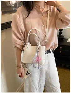 Stylish white woven bucket bag with heart charm and crossbody strap for women daily commute.