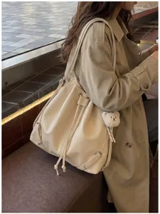 Vista detallada de una elegante mochila cubo en color beige con dije de osito y cordón.