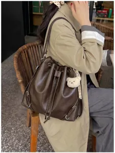 Vista detallada de una mochila de cubo de cuero marrón retro con cordón y colgante de oso.