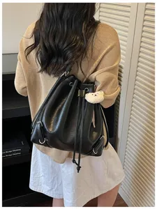 Mochila saco de cuero PU negro con cordón y colgante oso, vista detallada para uso diario urbano.