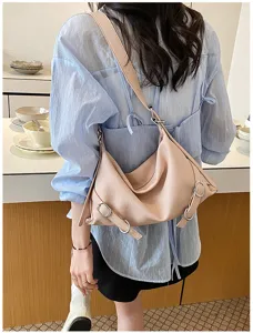 Détail élégant de sac porté épaule rose avec design souple et boucles métalliques.