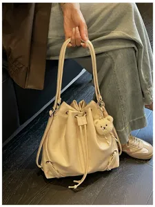 Vista detallada de la mochila tipo cubo crema con material suave y bonito colgante de oso.