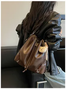 Vista detallada de la mochila de cuero marrón con colgante de oso y cordón ajustable.