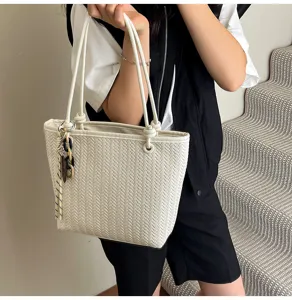 Detailed view of white woven tote bag with shoulder straps and chic hanging charm accessory.