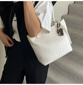 Detail view of white woven tote bag featuring chic chocolate pendant and shoulder style.