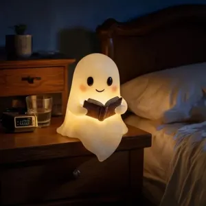 Vista detallada de una linda luz nocturna de fantasma leyendo un libro en la mesita.