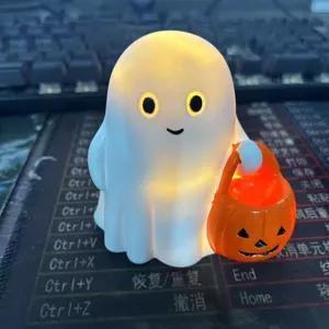 Cute white ghost night light figurine holding an orange pumpkin bucket on a desk.