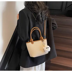 Detailed view of the woven bucket bag with brown leather handle and cute plush charm pendant.
