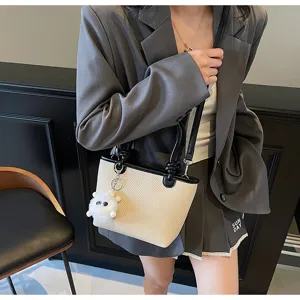 Woven bucket bag detail showcasing texture, black leather trim, and cute plush charm pendant.