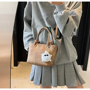 Detailed closeup view of stylish brown leather bucket bag featuring a cute fluffy monster charm.