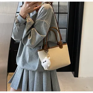 Detailed view of women's woven bucket bag with brown leather trim and cute plush pendant.