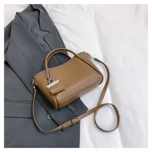 Detail view of brown leather handbag with strap and cute pendant, styled on grey blazer.