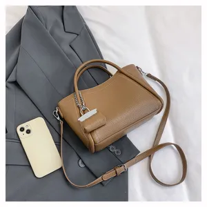 Detail view of stylish brown leather handbag with chain charm, laid out on blazer for daily use.