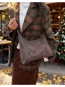 Close-up detail of retro brown suede shoulder bag with contrast white stitching and hardware.