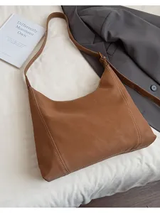 Detailed view of brown leather hobo shoulder bag with contrast stitching, styled on sheet.