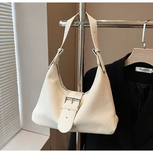 Close-up detail of the off-white textured shoulder bag hanging on a rack with a black jacket.