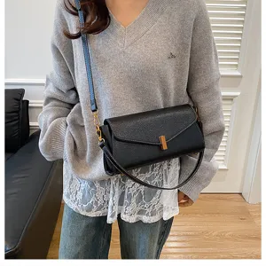 Black leather shoulder bag detail, stylish crossbody flap bag with metal clasp and thin strap.