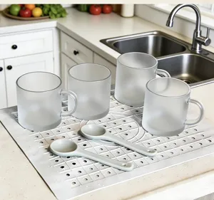Silicone draining mat set with frosted glass mugs and spoons for kitchen countertop use.