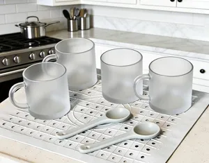 Detailed view of frosted glass mugs and spoons arranged on a kitchen silicone drying mat.