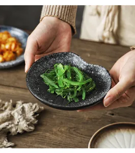 Macro view of a rustic black speckled ceramic saucer held by hands with seaweed salad