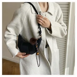Gros plan sur le sac porté épaule croissant noir élégant avec bandoulière nouée et pompon.