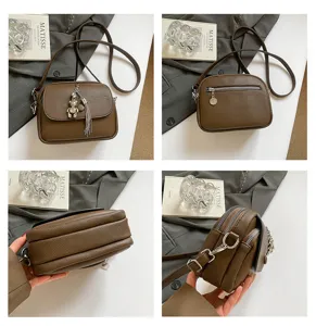 Detail view of brown leather crossbody bag featuring multi-compartment zippers and cute bear pendant.