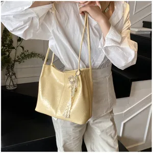 Detail shot of a stylish yellow crinkled tote bag with pearl pendant, perfect for daily commuting.
