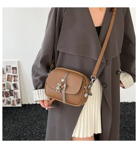 Detail shot of stylish brown crossbody bag with tassel and cute bear pendant charm.