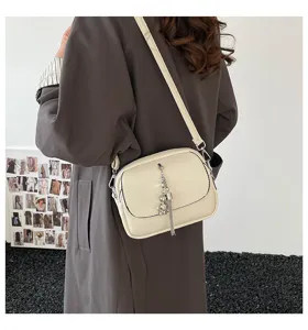Detailed view of women's minimalist beige crossbody bag with metal tassel and cute bear charm.