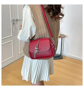 Red leather crossbody bag detail, featuring a cute bear pendant and chic metal tassel charm.