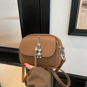 Stylish brown leather crossbody bag featuring metal tassel and cute bear pendant for women.