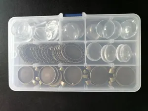 DIY jewelry making kit with bronze pendant trays and clear glass cabochons in a storage box.
