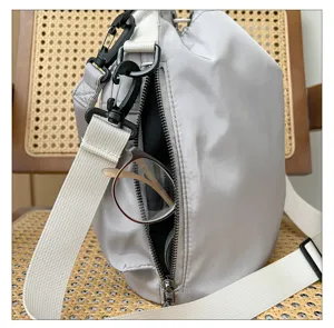 Casual light grey nylon crossbody shoulder bag with white strap and side zipper pocket detail.
