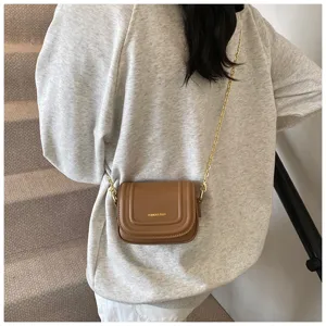 Detail shot of a stylish brown mini cross-body bag featuring a chic gold chain strap.