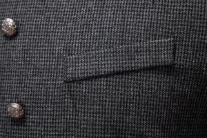 Detalle de chaqueta de traje para hombre, tejido texturizado de tweed gris con botones metálicos.